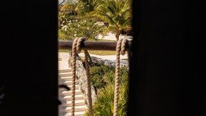A view through a window with a rope barrier, featuring a coastal landscape with mountains, a body of water, and palm trees. - The Dream | Private 360° View Suite in Buck Island (Buck Island)
