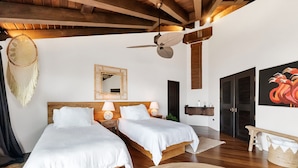 A bedroom with two beds, a ceiling fan, a mirror, and a painting.