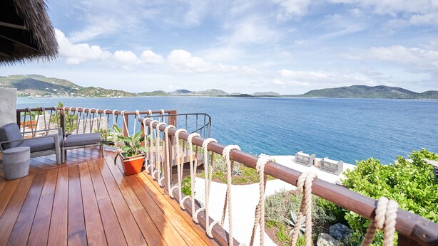 A wooden deck with a railing, a seating area, and a potted plant.