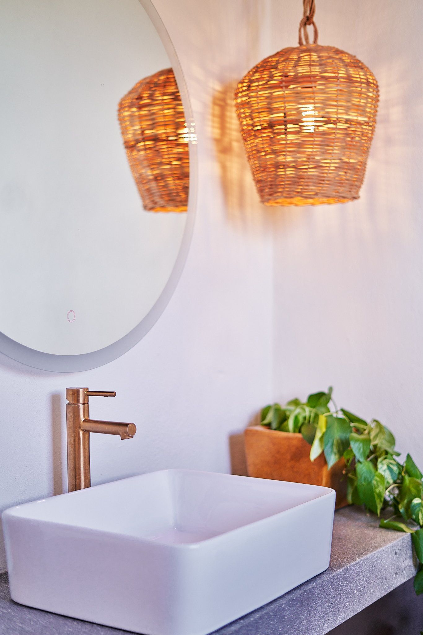 Une salle de bain avec un lavabo blanc, un miroir rond et un luminaire en osier.