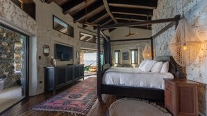Une chambre spacieuse avec un grand lit, un mur en pierre, un plafond en bois et une vue sur l’extérieur.
