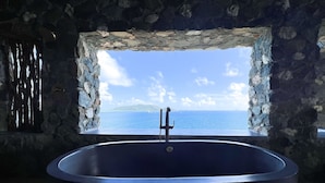 Une salle de bain aux murs de pierre, dotée d’une grande baignoire et offrant une vue sur la mer.