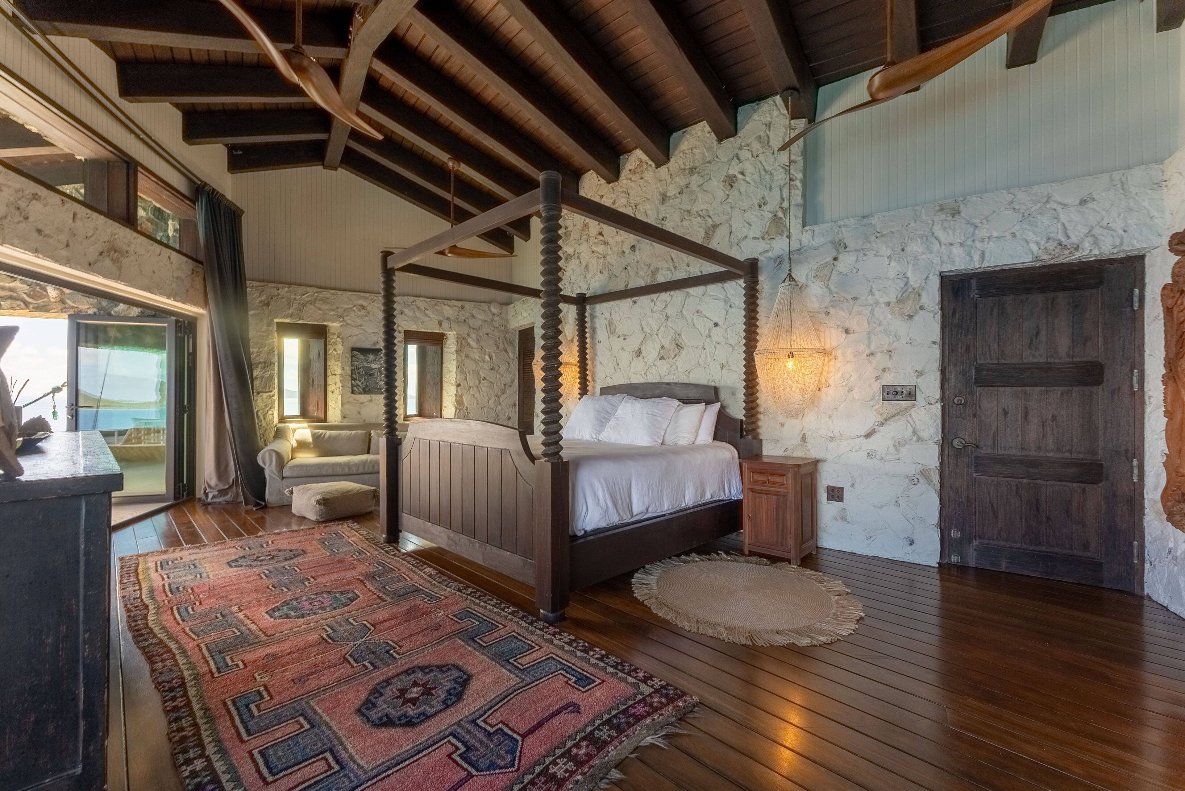 Una camera da letto con un letto a baldacchino, una parete in pietra, pavimento in legno e vista attraverso una porta di vetro.