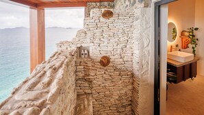 A stone-walled bathroom with a view of the sea, a wooden bench, and a sink with a mirror and plant. - Breakfast Incl | Caribbean Escape | Ocean Views (Buck Island)