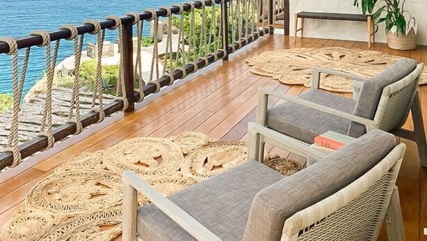 A wooden deck with wicker furniture and a view of the ocean.