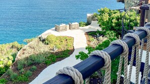 A coastal view with a thatched-roof structure, a stone pathway, and a rope barrier.