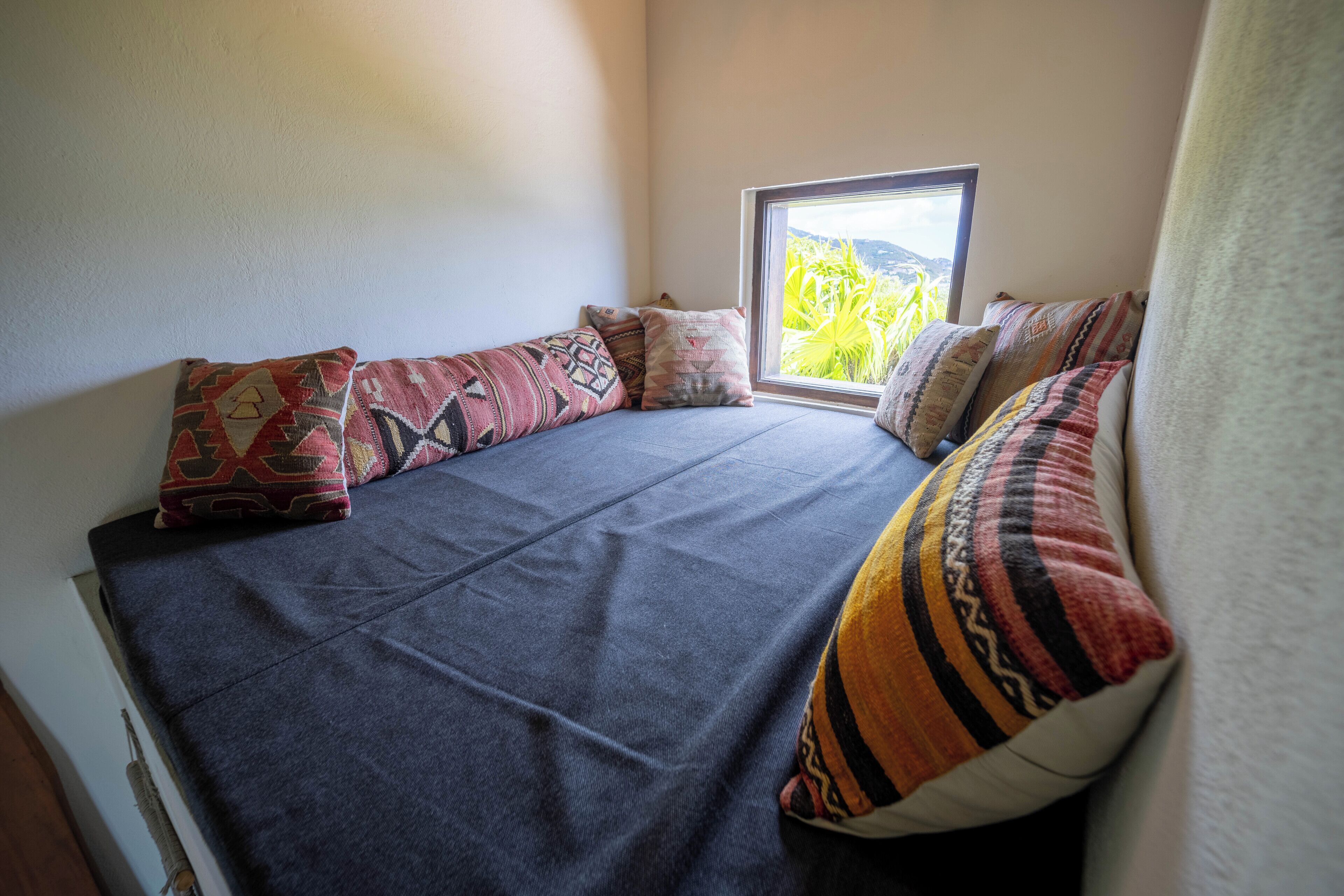 Une pièce confortable avec un lit, des oreillers et une fenêtre donnant sur un paysage verdoyant.