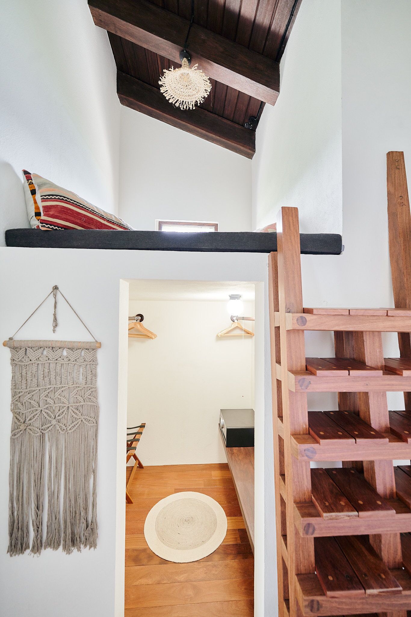 Un escalier en bois, agrémenté d’une décoration murale en macramé et d’un tapis tissé sur le sol.