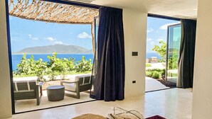 Una habitación moderna con un gran ventanal corredero que da a una zona de estar exterior con vistas al mar y a las montañas.