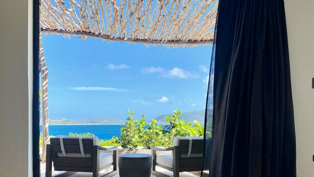 Una habitación con vista al mar, un reposapiés de mimbre y una mesa de centro negra.
