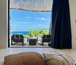 Una habitación con vista al mar, un reposapiés de mimbre y una mesa de centro negra.