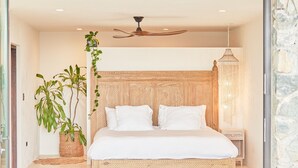 Un dormitorio con una cama grande, dos sillas blancas, una mesita y plantas en macetas.