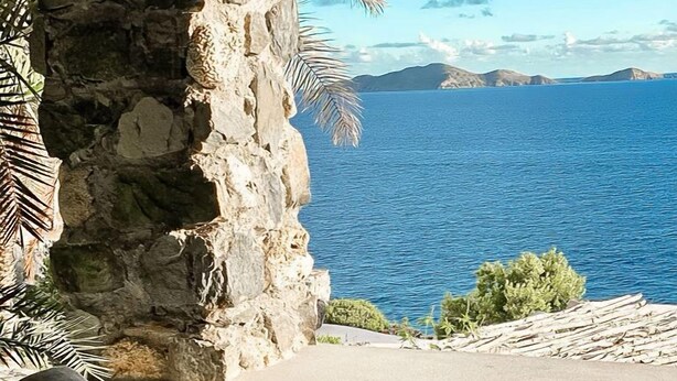 Un mur de pierres offrant une vue sur la mer, une chaise en bois et une petite table.