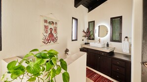 Une salle de bain moderne avec un lavabo blanc, des meubles en bois foncé, un ventilateur de plafond et un tapis rouge à motifs.