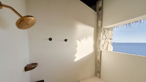 Une salle de bain avec douche, une fenêtre donnant sur la mer et un mur en pierre.