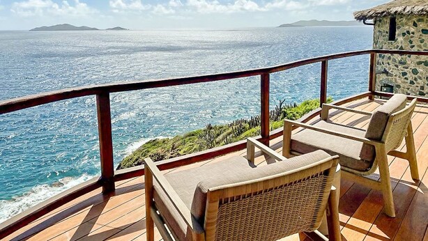 Une terrasse en bois avec des fauteuils en osier, offrant une vue sur la côte.