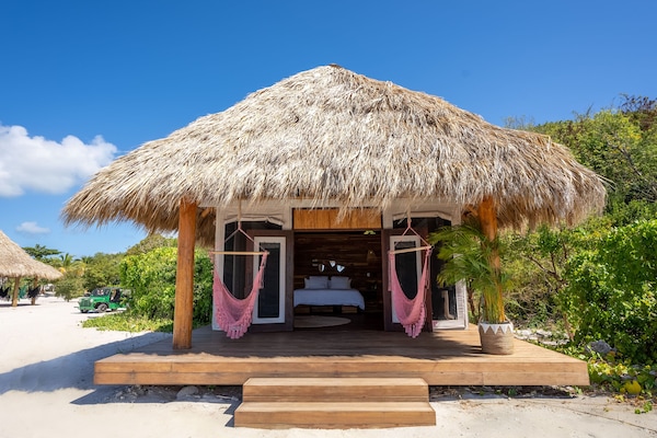Thatched-roof beachfront teepee nestled in tropical greenery with hammock swings.