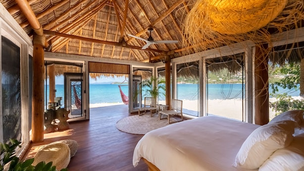 A spacious room with a large bed, a ceiling fan, and a view of the beach. - Secluded Beachfront Teepee Villa w/ Ocean Views (Buck Island)
