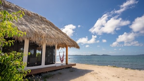 A beachside hut with a thatched roof, wooden deck, and a hammock. - Secluded Beachfront Teepee Villa w/ Ocean Views (Buck Island)