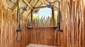 A room with a thatched roof, bamboo walls, and a central shower area with two overhead showerheads. - Secluded Beachfront Teepee Villa w/ Ocean Views (Buck Island)