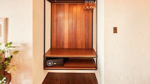 Un banco de madera con una lámpara colgante de fibras tejidas arriba, una lámpara de pared y una planta a la izquierda.