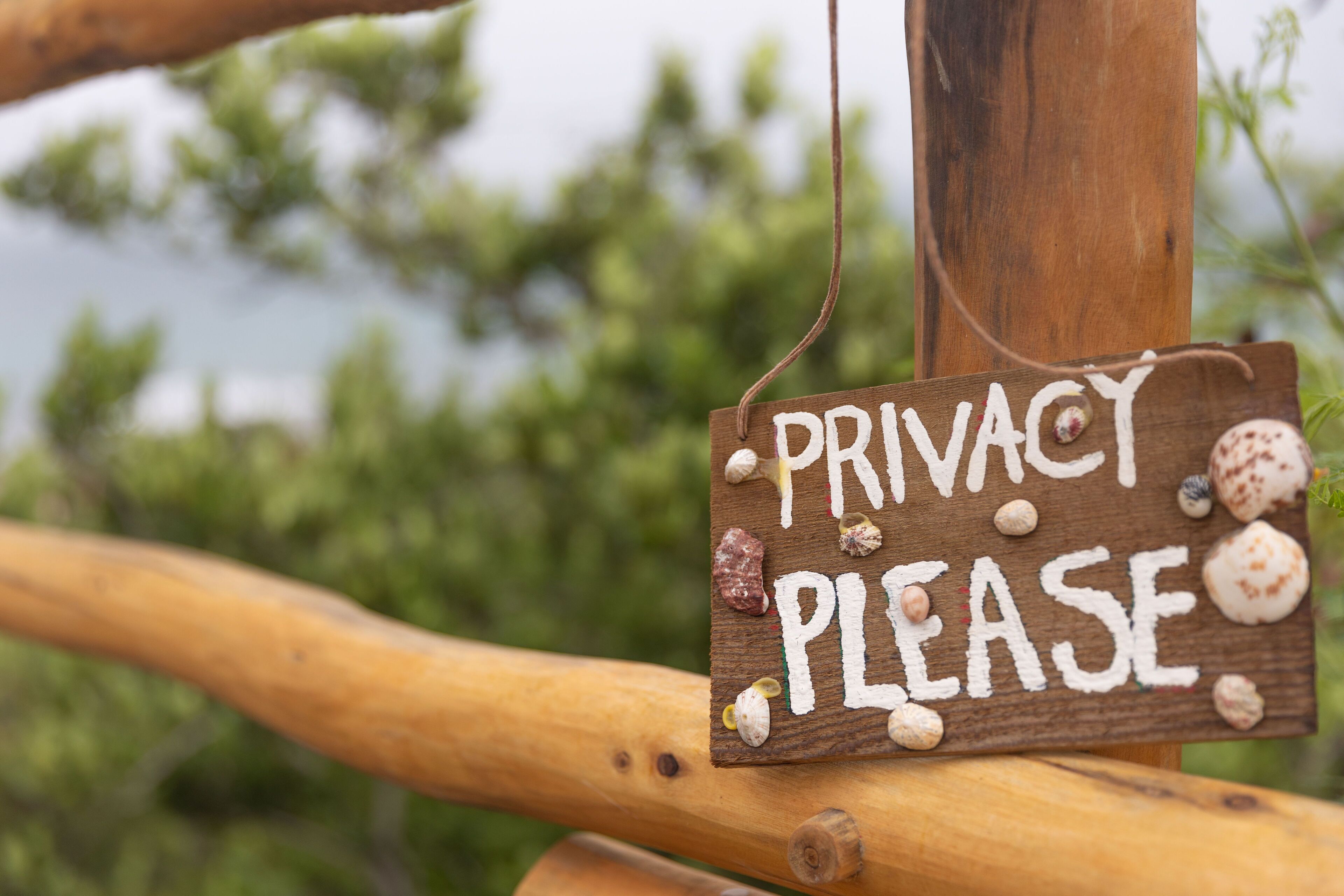 Een houten bord met de tekst 'PRIVACY PLEASE' en er zitten schelpen aan bevestigd.