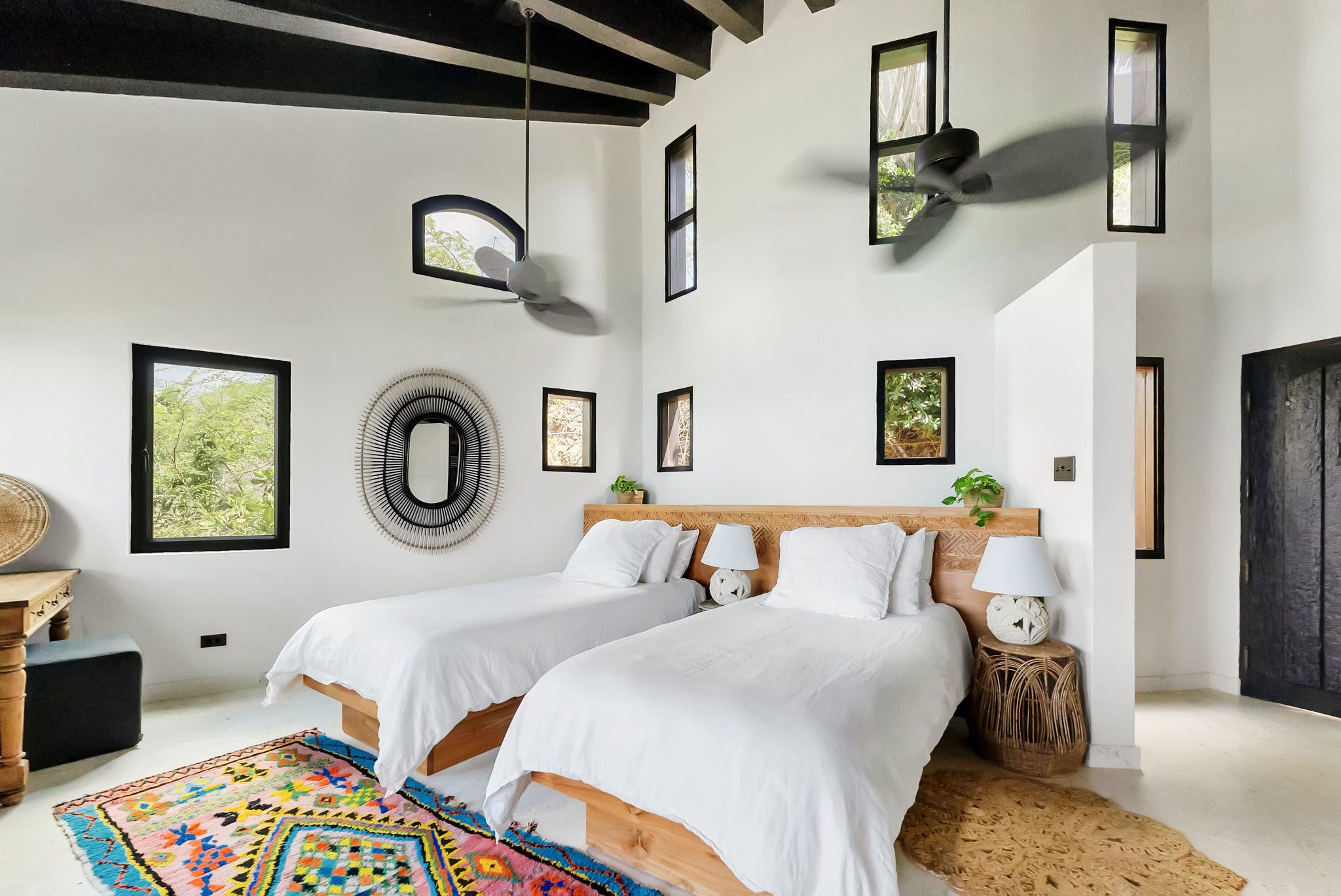 A modern bedroom with two beds, a large mirror, and multiple windows.