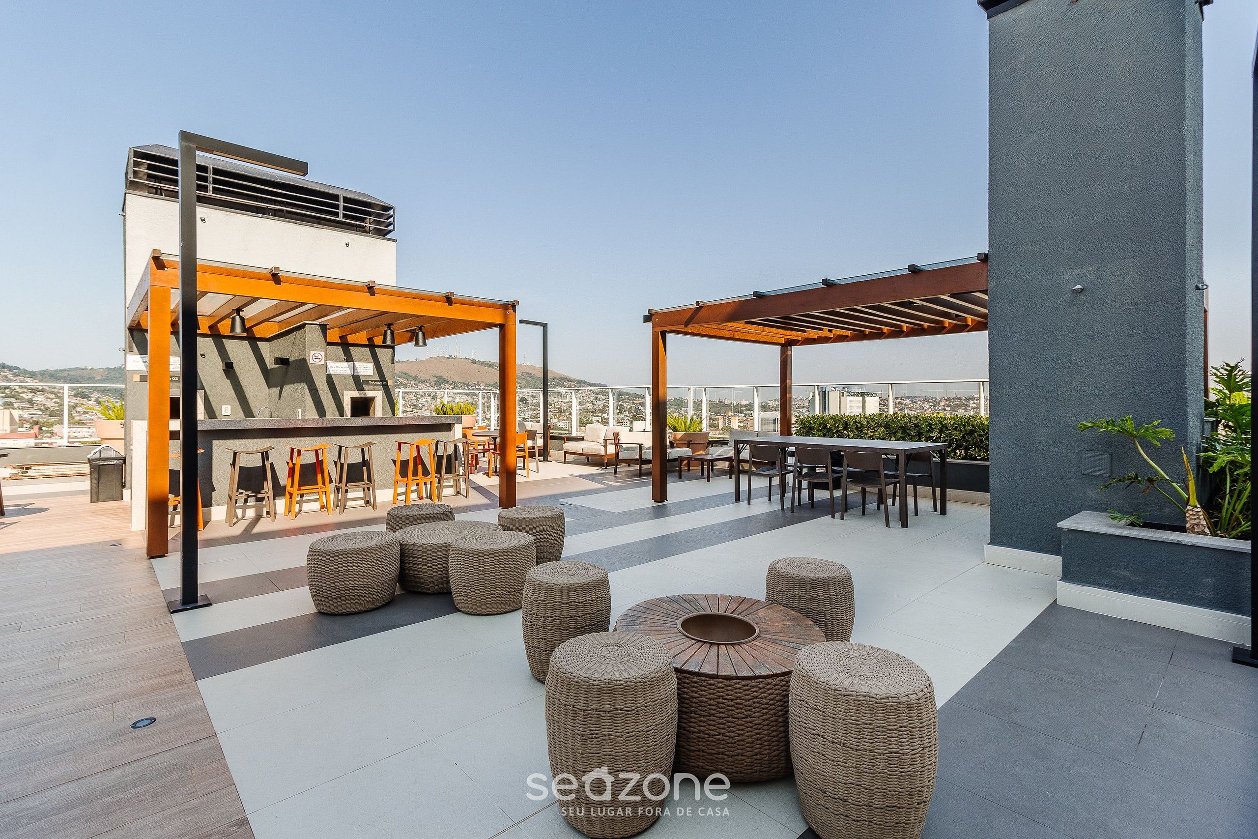 Un patio al aire libre con mobiliario de mimbre, un pérgola y vistas a la ciudad.