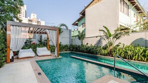 A swimming pool with a pergola and lounge chairs, surrounded by greenery and a building. - Studio in Building With Pool Con1206 (Porto Alegre)