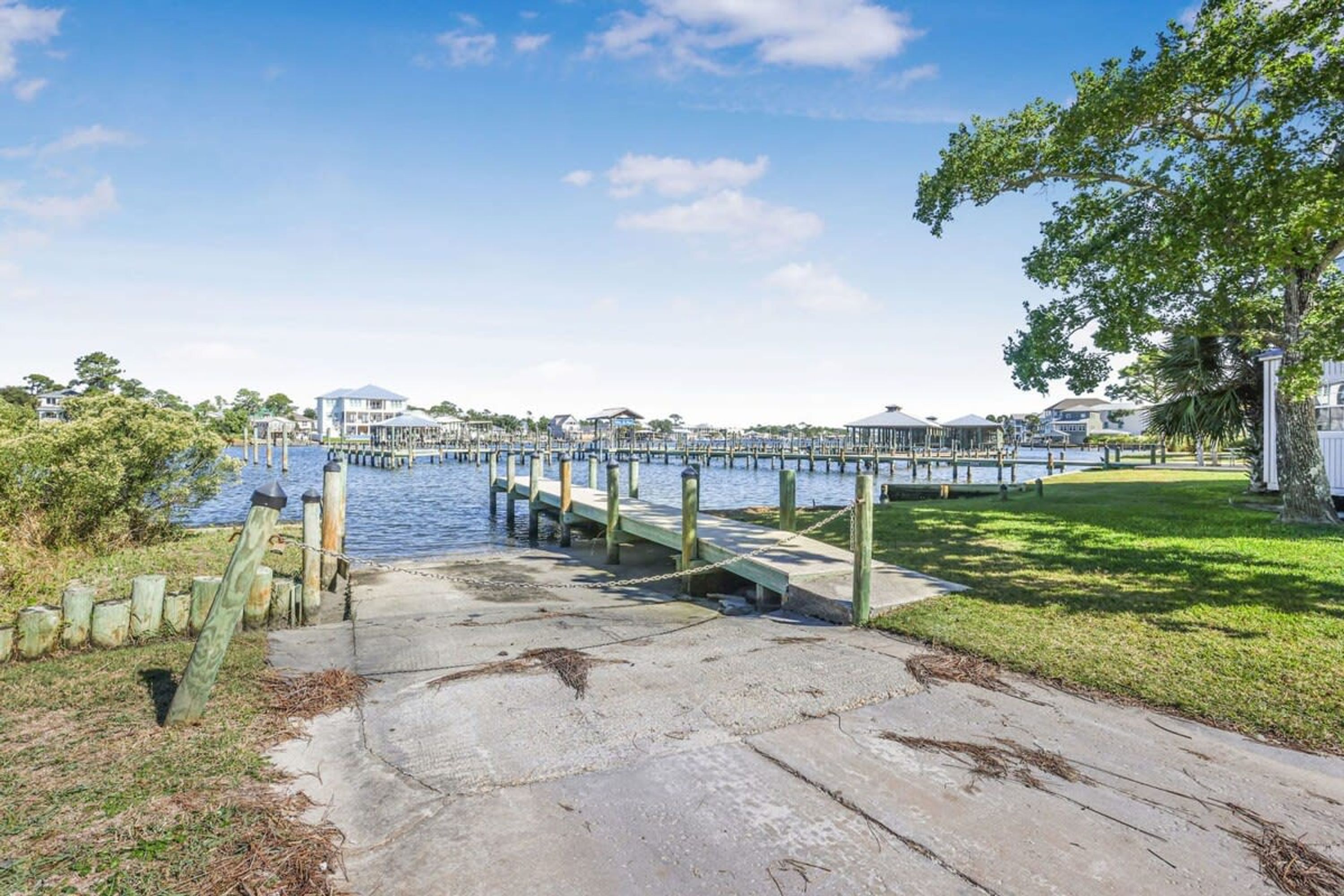 A waterfront property with a concrete dock leading to a pier, surrounded by greenery and a clear sky.