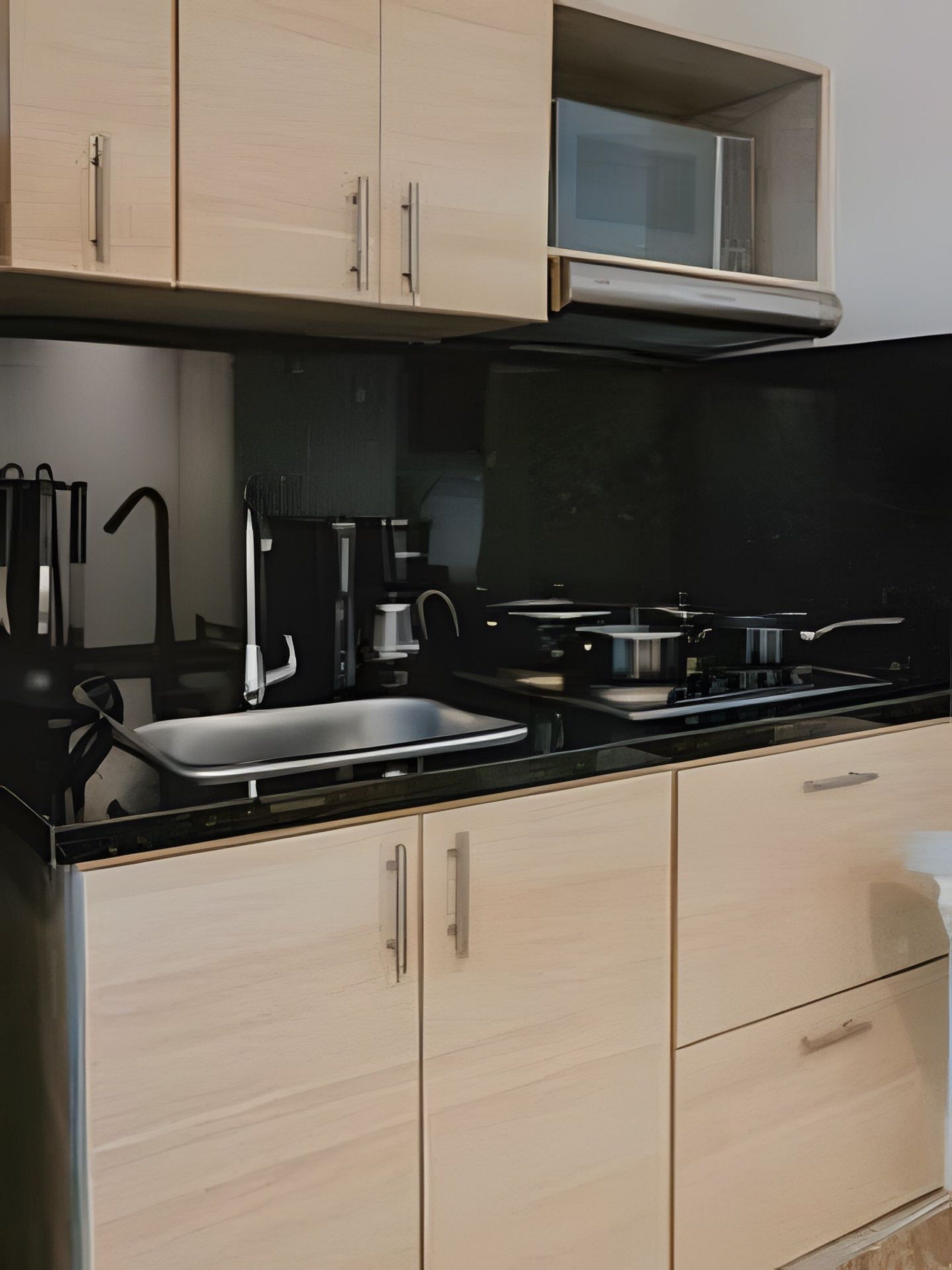 A modern kitchen with light wood cabinets, a black countertop, and stainless steel appliances.