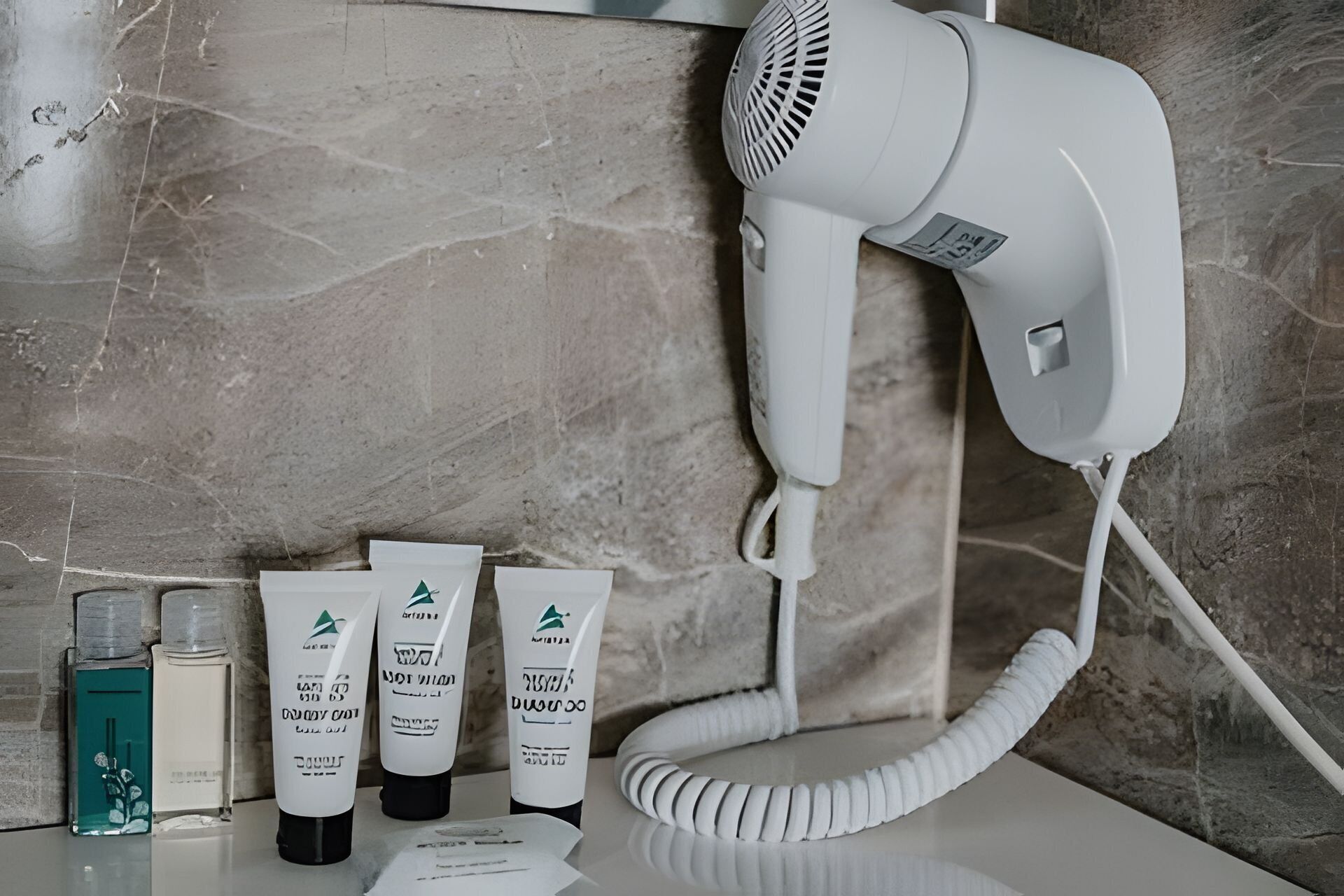 A hairdryer on a wall, three hair care products, and a blue bottle on a counter.