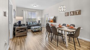 Un salon moderne avec un coin repas, comprenant un ensemble de canapés, une table à manger en bois avec des chaises et une œuvre d’art murale.