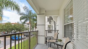 Un balcon avec une table et des chaises, un pot de fleurs et une vue sur la rue et les immeubles.