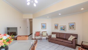 A living room with a brown sofa, two armchairs, a glass coffee table, and a TV. There are three framed paintings on the wall. - 3BR Seafront apt w/ BBQ in Itapema Con0101 (Itapema)
