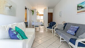 Ein Wohnzimmer mit einem weißen Sofa, einem grauen Sofa mit blauen Kissen und einem Essbereich mit Tisch und Stühlen.