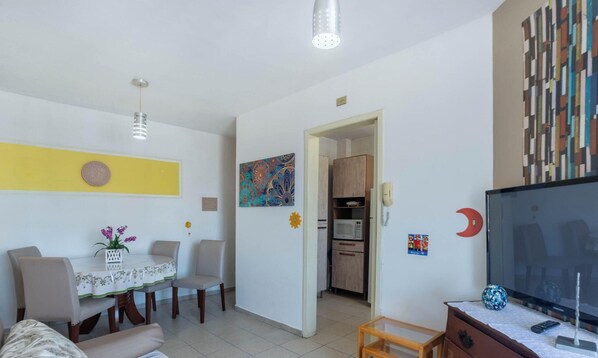 A modern living room with a dining area, a TV, and a kitchen in the background.