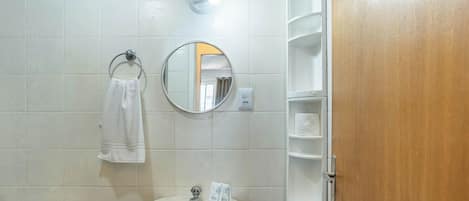 A bathroom with a white sink, a round mirror, a towel hanging on a metal ring, and a wooden door.