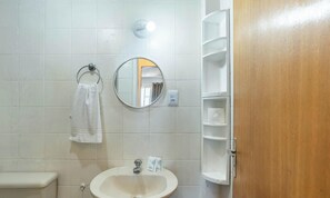 Une salle de bain avec un lavabo blanc, un miroir rond, un porte-serviettes et une porte en bois.