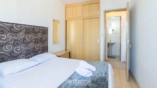 Een slaapkamer met een bed, een kledingkast, een nachtkastje en een badkamer die door een open deur zichtbaar is.