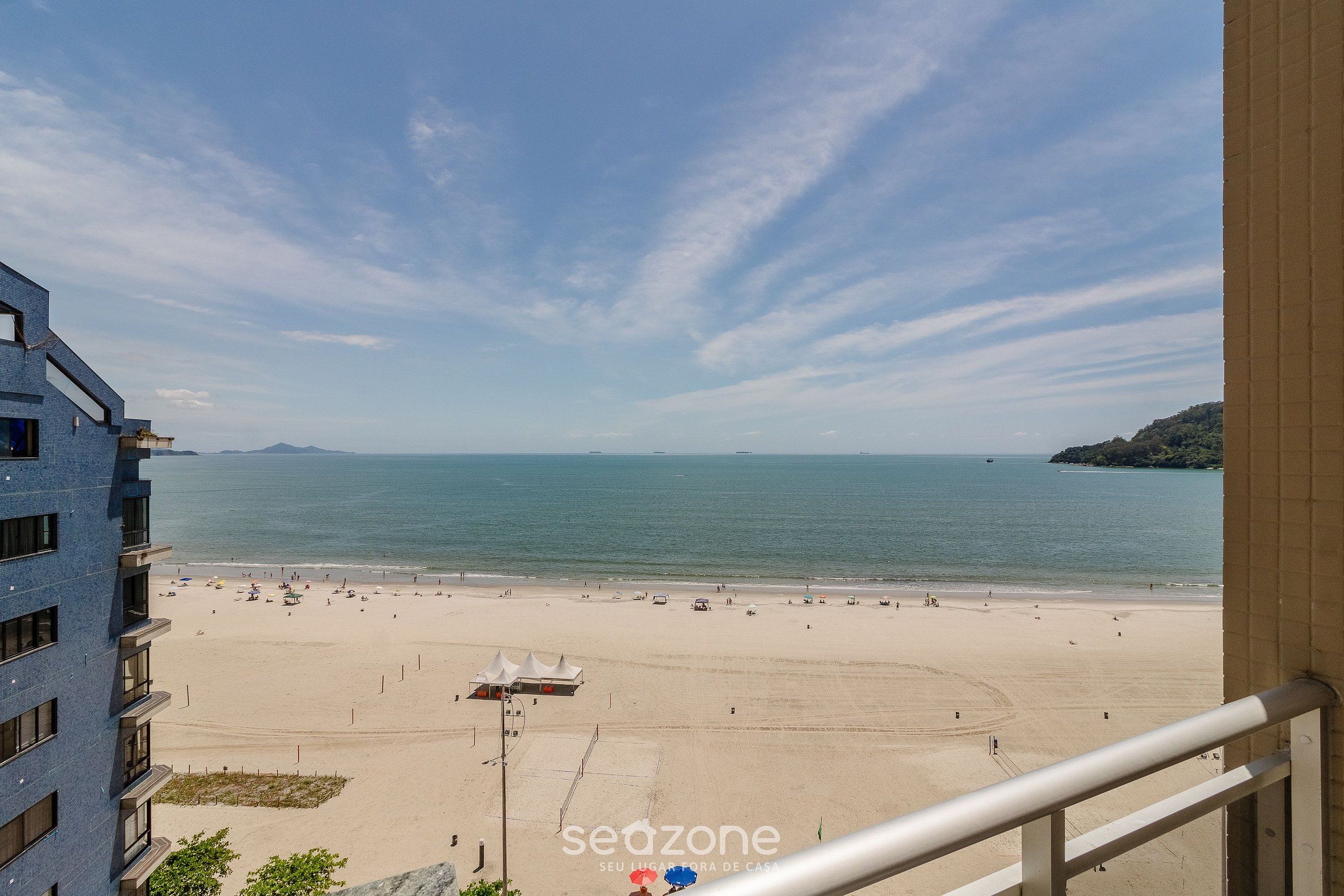Blick auf einen Strand vom Balkon aus, mit blauem Himmel, sandigem Strand und einem fernen Gebirge.