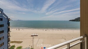 A beach view from a balcony with a clear sky, a sandy beach, and a distant mountain. - 3BR Beachfront apt w/ sea View Cet802 (Balneário Camboriú)