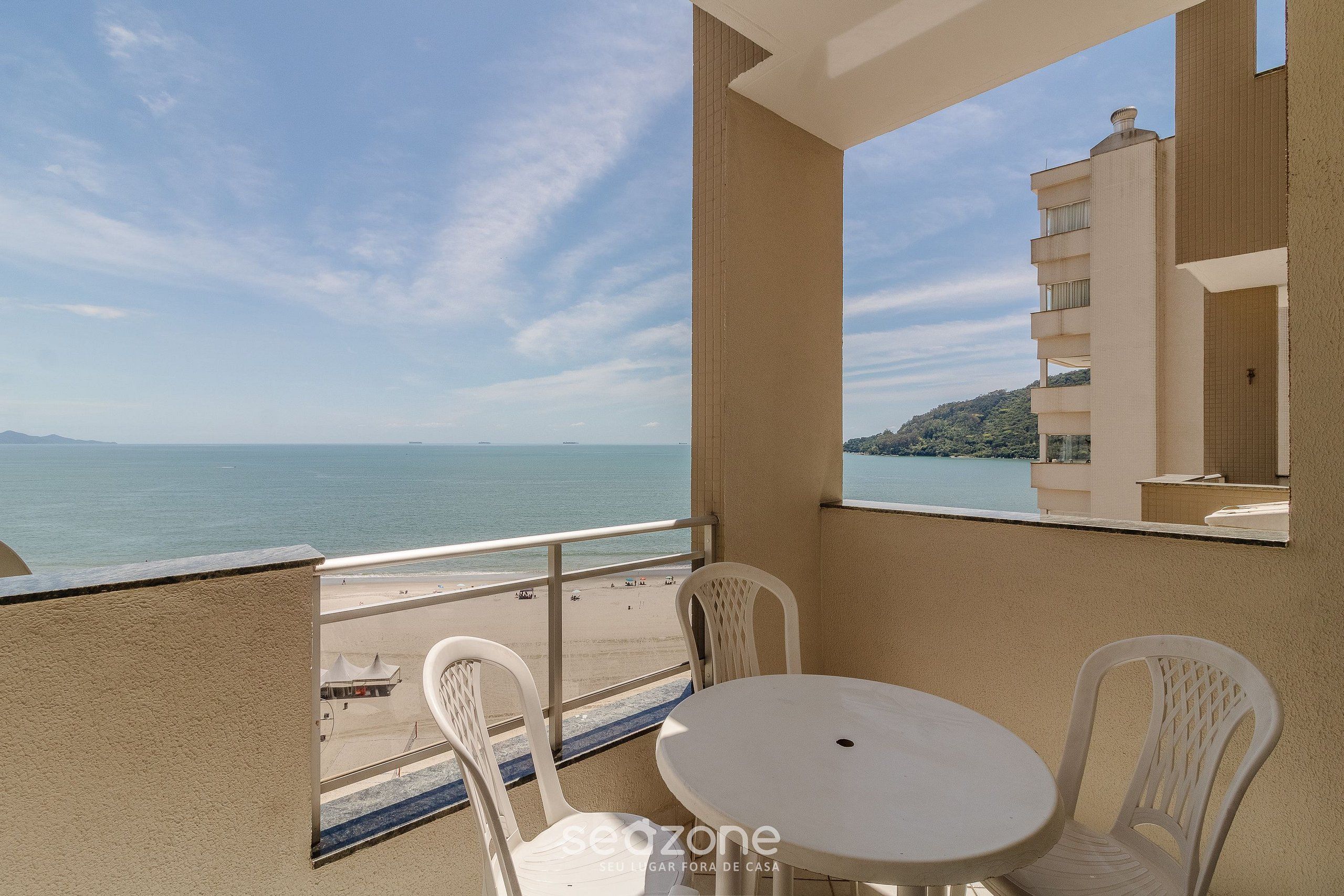 Ein Balkon mit Blick aufs Meer, ein weißer Tisch und weiße Stühle.