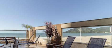 Una terraza con sillas de mimbre y una planta en maceta, con vista a una playa y una montaña.