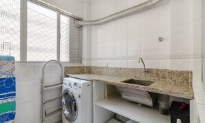 Une buanderie équipée d’un lave-linge, d’un évier et d’une fenêtre avec des stores.