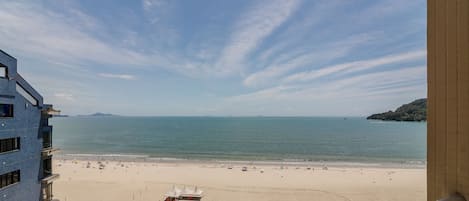 A beach view from a balcony with a clear sky, a sandy beach, and a distant mountain.