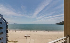 Une vue sur la plage depuis un balcon, avec un ciel dégagé, une plage de sable et une montagne lointaine.
