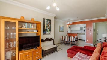 A living room with a TV, wooden cabinet, red sofa, and a dining area with chairs and a table.