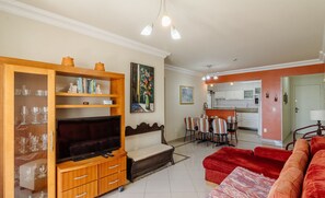 Un salon avec un téléviseur, un meuble en bois, un canapé rouge et un coin repas comprenant des chaises et une table.