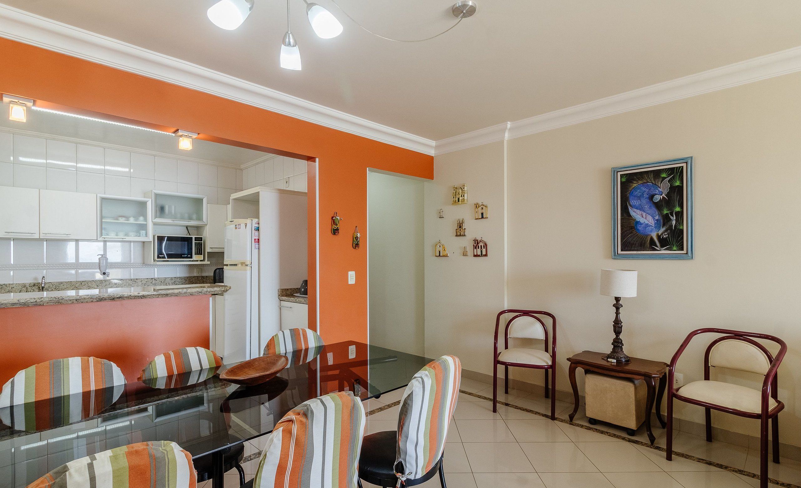 Un comedor con mesa de vidrio, sillas a rayas, una lámpara y un cuadro en la pared.